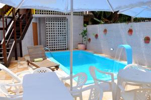 a swimming pool with white chairs and an umbrella at Paranambuca Pousada in Porto De Galinhas