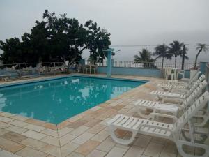 ein Pool mit weißen Liegestühlen daneben in der Unterkunft 27 Praia Hotel - Frente Mar in Bertioga