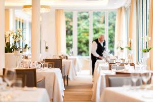 un hombre de pie en un comedor con mesas en Hotel Mignon Meran Park & Spa, en Merano