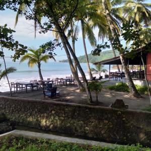 einen Strand mit Tischen, Palmen und dem Meer in der Unterkunft Kuda Laut Resort in Cisolok