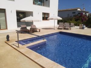 a swimming pool with chairs and umbrellas next to a house at Apartamentos Villa Primera in Cala Figuera