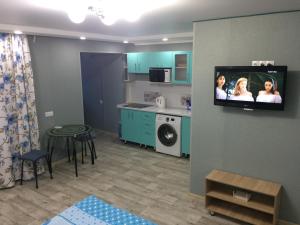 a living room with a kitchen and a tv on a wall at Apart Auezov street City Centr in Ustʼ-Kamenogorsk