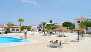 a swimming pool with chairs and umbrellas and people sitting at New renovated duplex near the ocean located in Tenerife Sur in Costa Del Silencio