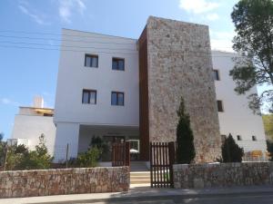 a large white building with a stone wall at Apartamentos Villa Primera in Cala Figuera