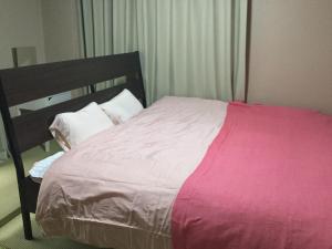 a bedroom with a large bed with pink sheets and pillows at Kurosaki Guesthouse 403 in Kitakyushu