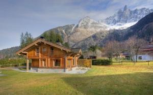 una cabaña de madera en un campo con montañas al fondo en Chalet Bois - Chamonix, en Chamonix-Mont-Blanc