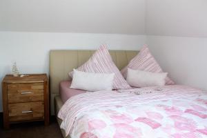 un letto con lenzuola rosa e bianche e un comodino in legno di Ferienwohnung Hermann-Daur-Weg a Cuxhaven