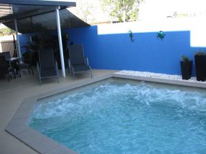 a large swimming pool with chairs and a blue wall at Charm City Motel in Bundaberg