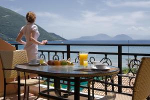 a woman standing on a balcony looking out at the ocean at Hotel Grand Nefeli in Vasiliki