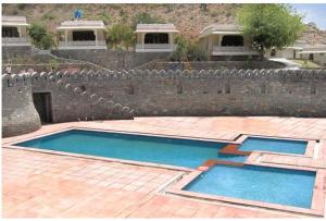 2 piscinas en un patio con una pared de piedra en Devi Palace Resort, en Kumbhalgarh