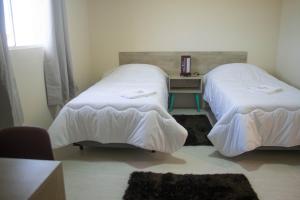 two beds in a small room with a desk and a bed at Hotel Marrocos in Pelotas