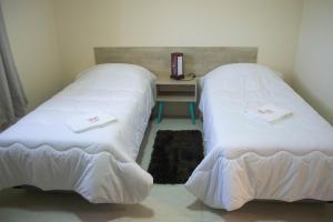 two beds in a room with a table with a book at Hotel Marrocos in Pelotas