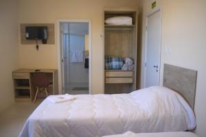 a bedroom with a white bed and a desk and a desk at Hotel Marrocos in Pelotas