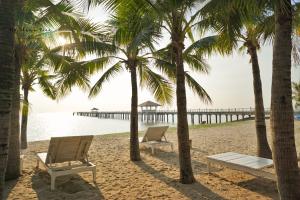 two chairs and palm trees on a beach with a pier at Villa at Casalunar Bangsaen in Bangsaen
