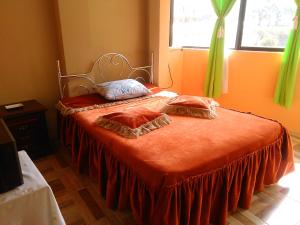 a bed with an orange blanket and two pillows on it at Casa Huespedes El Molino in Tababela