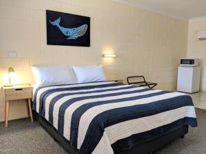 a bedroom with a bed with a blue and white striped blanket at Sail Inn Motel in Yeppoon