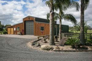 a wooden building with a garage and palm trees at Pickering Barn Stay in Tamahere