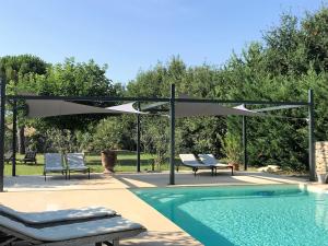 a swimming pool with two chairs and a canopy over it at Mas Oréa Sous la glycine in Gordes