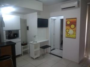 Eine weiße Küche mit Schreibtisch und Fernseher an der Wand in der Unterkunft Aldeia das Águas Barrakana flats in Nossa Senhora das Dores
