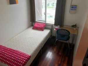a small room with a bed and a chair at Kumoji-so Hostel in Naha