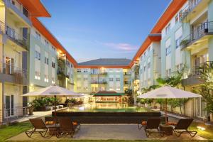 un patio con una piscina con sillas y sombrillas en HARRIS Hotel & Residences Riverview Kuta, Bali - Associated HARRIS, en Kuta
