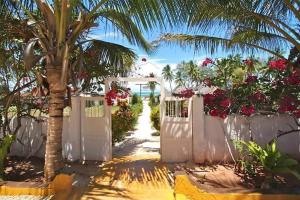 a white gate with a palm tree and flowers at Bahati Villa in Kiwengwa