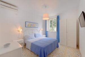 a white bedroom with a blue bed and a window at Le Querce in Procida