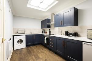 uma cozinha com armários azuis e uma máquina de lavar e secar roupa em The Old Station House - Stylish & Central 2BDR Apartment em Oxford