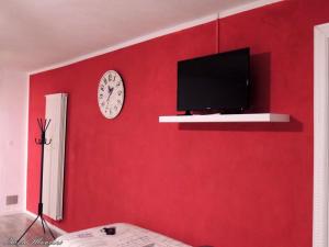 una parete rossa con TV e orologio di La Casa del Colonnello a Vercelli