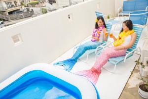 two girls sitting in chairs next to a swimming pool at Guesthouse TT Koza in Okinawa City