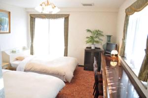 a bedroom with two beds and a table and a television at Green Hotel Rich Tokugawaen in Okazaki
