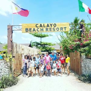 un grupo de personas de pie bajo un cartel de resort de playa en Calayo Beach Resort, en Nasugbu
