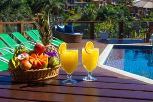 Dois copos de sumo e uma cesta de frutas numa mesa perto da piscina. em Coronado Inn Hotel em Búzios