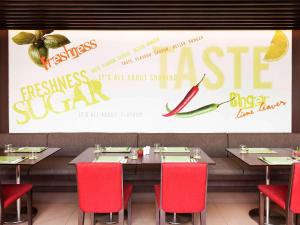 a restaurant with tables and red chairs and a large screen at Ibis Bangkok Riverside in Bangkok