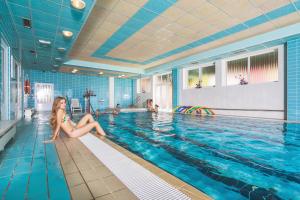 a woman sitting on the edge of a swimming pool at Hotel Ambra in Luhačovice +42 photos