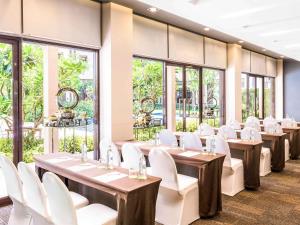 a room with tables and white chairs and windows at Ibis Bangkok Riverside in Bangkok
