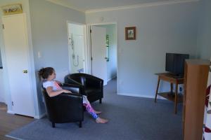 Ein kleines Mädchen auf einem Stuhl im Zimmer in der Unterkunft Smiths Farm Holiday Park in Linkwater