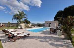 a swimming pool with wooden benches and tables next to it at Masseria Li Campi in Cavallino di Lecce