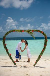 a couple kissing under a heart shaped arch on the beach at Biyadhoo Island Resort in Biyadhoo