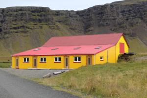 a yellow and red building on a hill next to a road at Lækjarhus Farm Holidays in Borgarhöfn