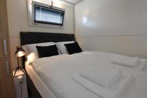 a white bed with black pillows and a window at Cosy floating boatlodge Athene in Maastricht
