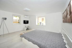 a white bedroom with a bed and a tv at Pure Apartman Pécs in Pécs