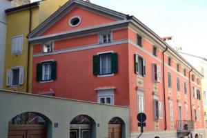 a red building with green shutters on a street at Madonna del Mare in Trieste