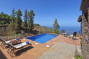 einen Pool mit Stühlen, einem Tisch und dem Meer in der Unterkunft Casa Antonia in Tijarafe