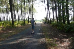 a man riding a skateboard with a dog on a path at Blue Ocean in Moliets-et-Maa