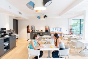 Dos mujeres sentadas en mesas en un restaurante en Hotel Enight en Gradignan