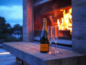 a bottle of wine and two wine glasses next to a fireplace at The Glasshouse in Whangarei Heads