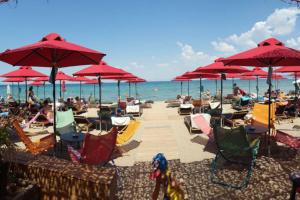 einen Strand mit Stühlen und roten Sonnenschirmen und dem Meer in der Unterkunft Apartment by the beach with amazing sea view in Peraia