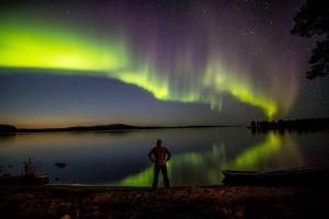 a man standing in front of a lake under the aurora at Wilderness Hotel Inari & Igloos in Inari