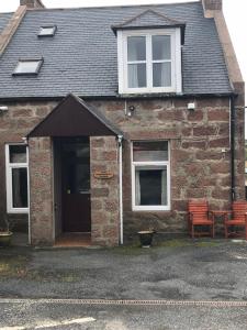 uma casa de tijolos com duas cadeiras e uma porta em Invernettie guesthouse em Peterhead